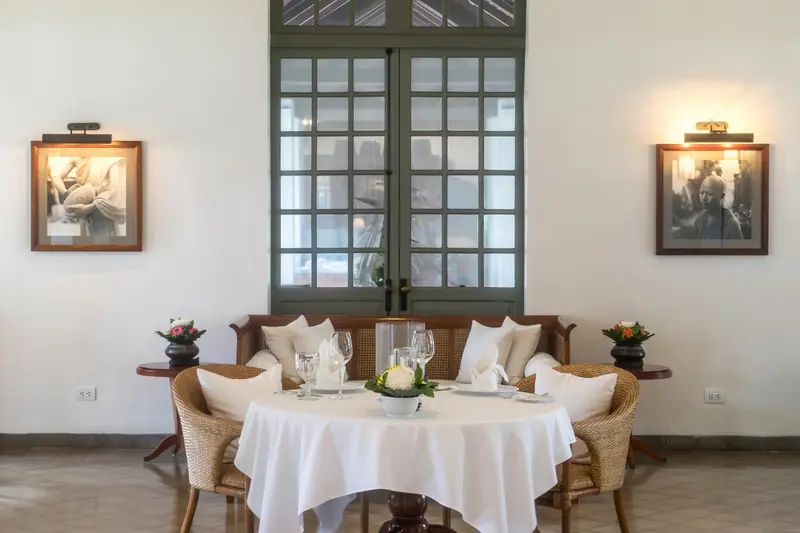 Round white-clothed table ringed by rattan armchairs in a bright dining room
