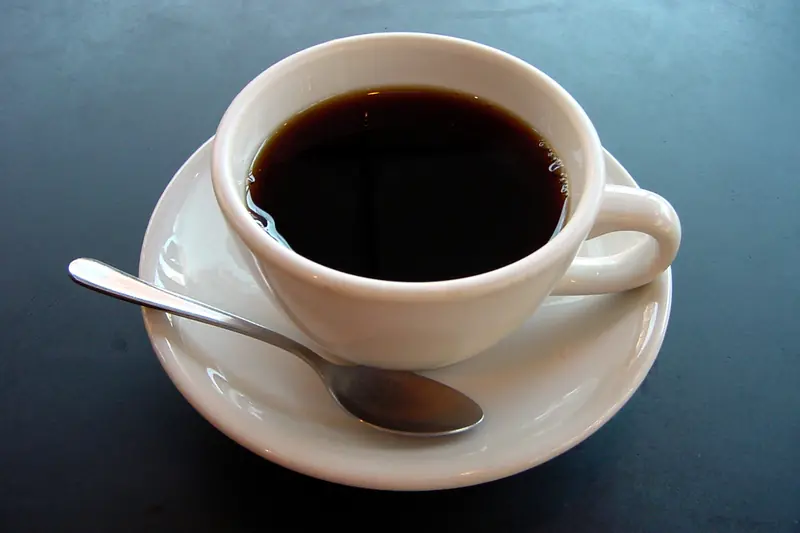 Tasse de café noir sur sa soucoupe avec une cuillère, sur une table bleu sombre