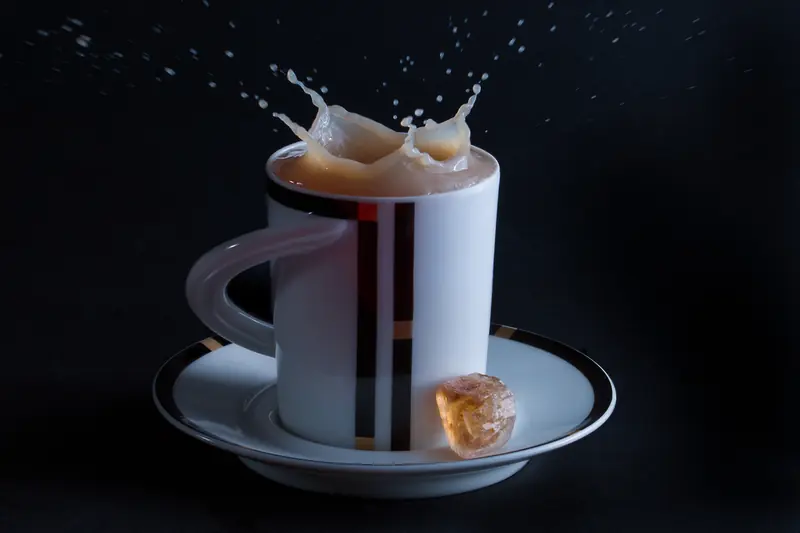 Striped white cup of milky tea, a lump of brown sugar sending up splashes against black