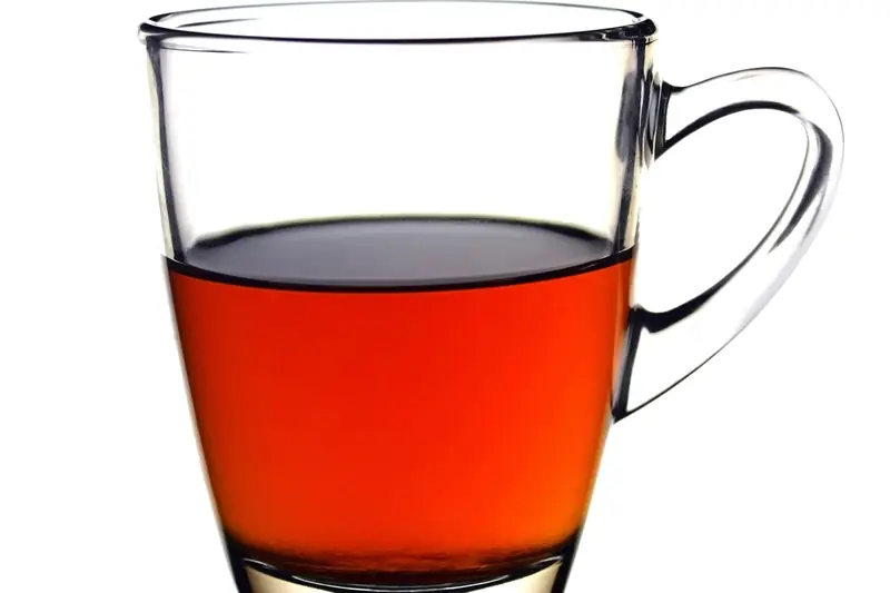 Tasse en verre de thé noir couleur ambre, isolée sur un fond blanc