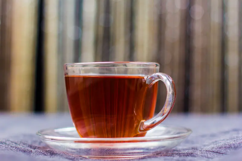 Glass cup of amber red tea on its saucer, with a bamboo screen in the background