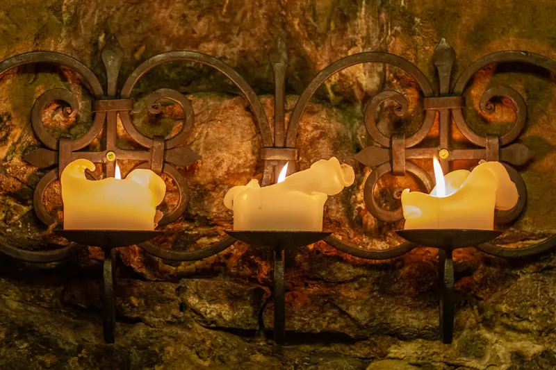 Three lit candles on a wrought-iron candelabra against a stone wall