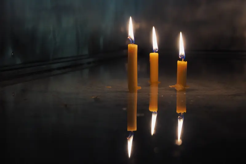 Three slender lit tapers mirrored in a dark, glossy surface below them