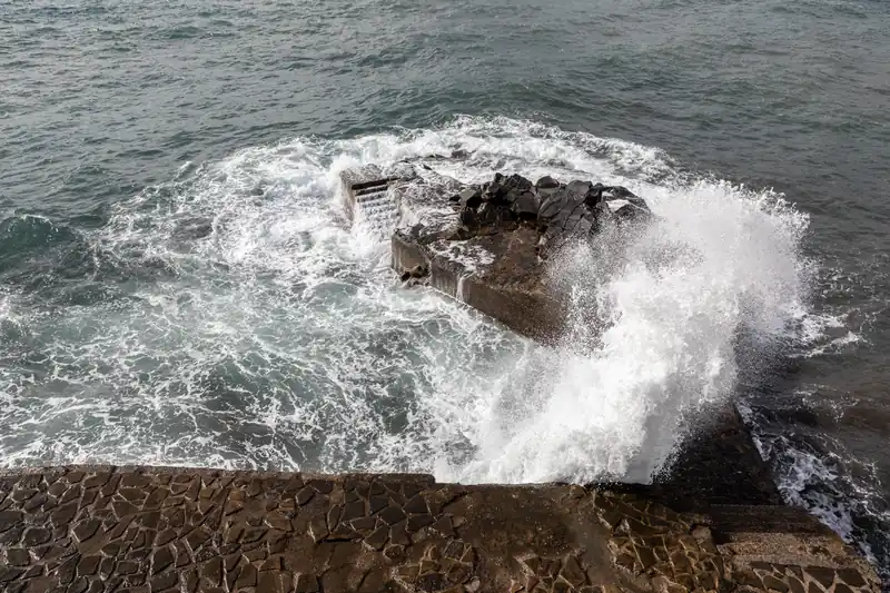 Vague qui recouvre un escalier de pierre volcanique au bord de l'océan, à Madère