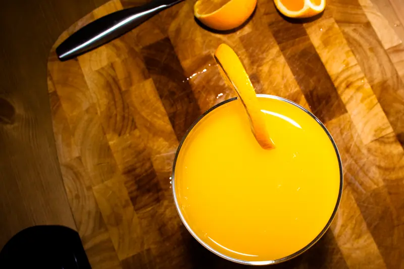 Verre de jus d'orange vu du dessus sur une planche en bois, avec des moitiés d'orange