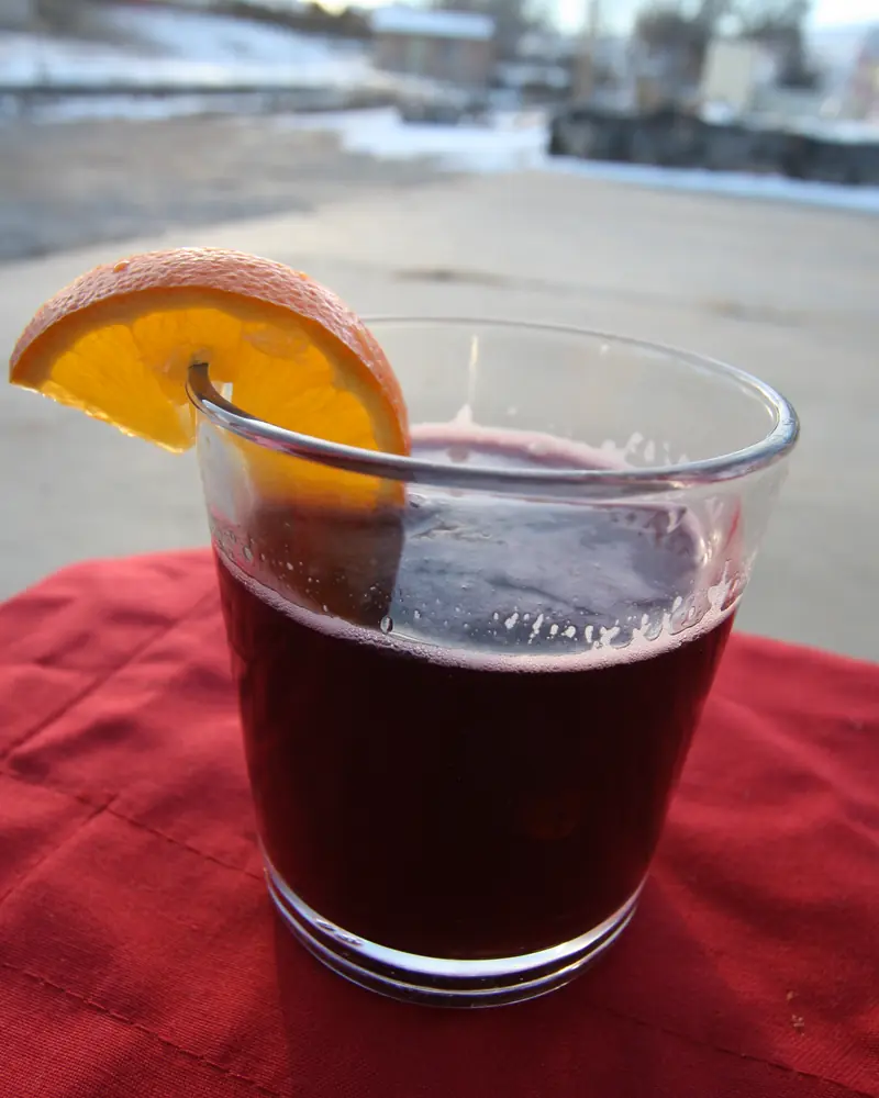 Verre de vin chaud garni d'une rondelle d'orange sur une nappe rouge, en hiver