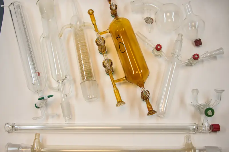 Verrerie de laboratoire transparente et ambrée disposée sur fond blanc : colonnes, ballons, robinets