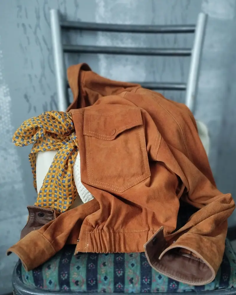 Veste en daim couleur cognac posée sur le dossier d'une chaise avec un foulard