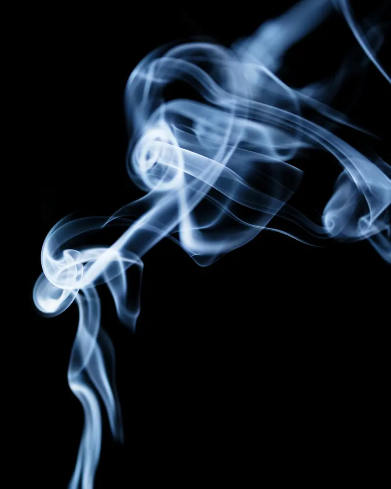 Volute de fumée bleutée qui s'élève d'un bâton d'encens sur fond noir